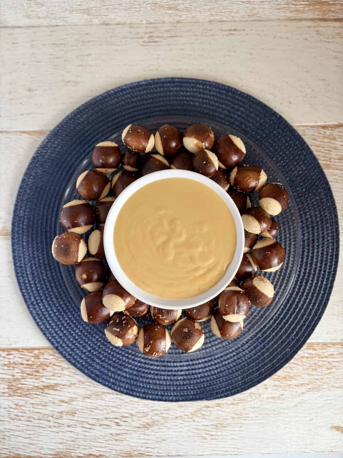 Beer Cheese Dip in a white bowl surrounded by pretzel bites on a plate.