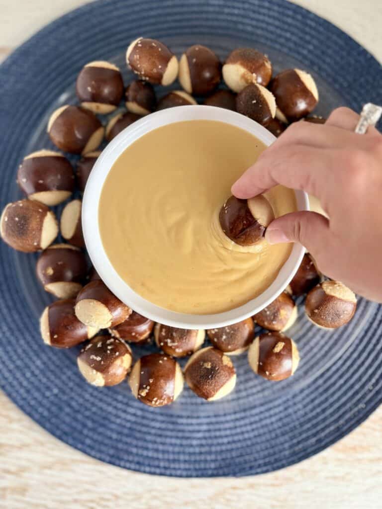 Creamy beer cheese dip surrounded by pretzel bites on a blue plate, perfect for snacking and party appetizers.