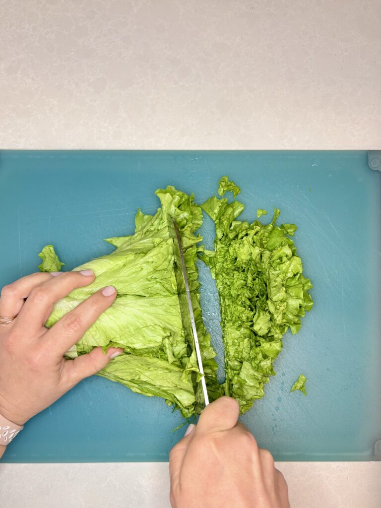 lettuce being chopped into small pieces on a cutting board with a knife