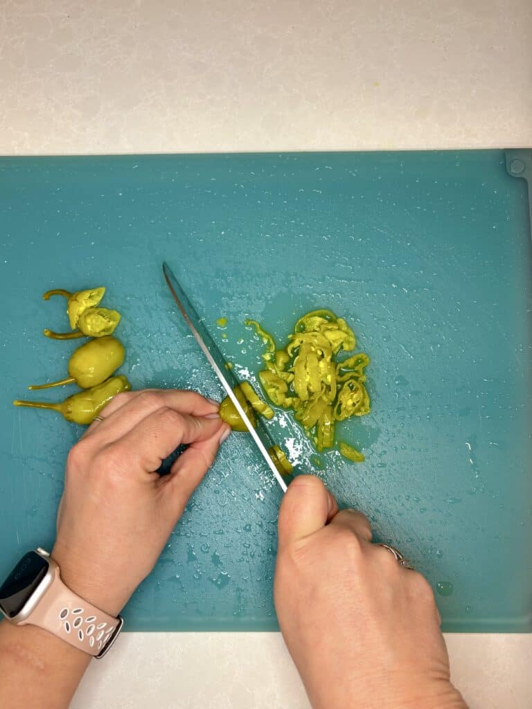 greek peppers being sliced on a cutting board with a knife