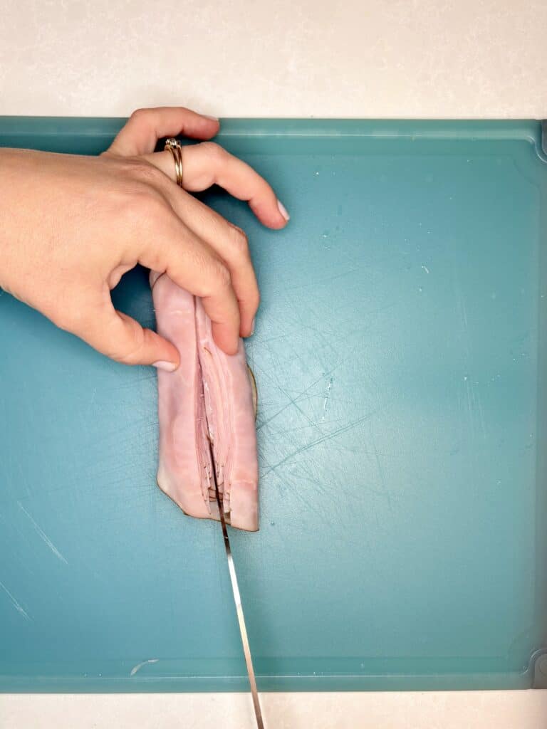 rolled up ham being sliced on a cutting board 