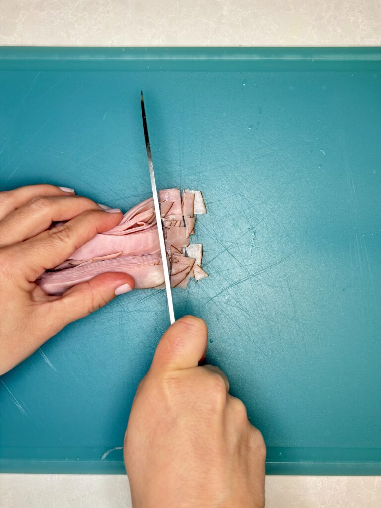 rolled up ham being diced into small pieces on a cutting board 