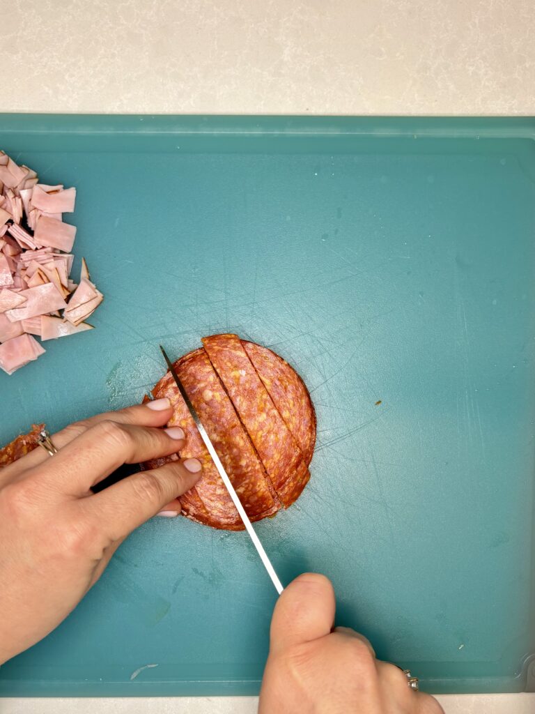 pepperoni being sliced into strips on a cutting board 