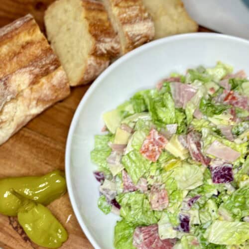 chopped antipasto salad in a meal bowl on a cutting board with a loaf of sliced bread