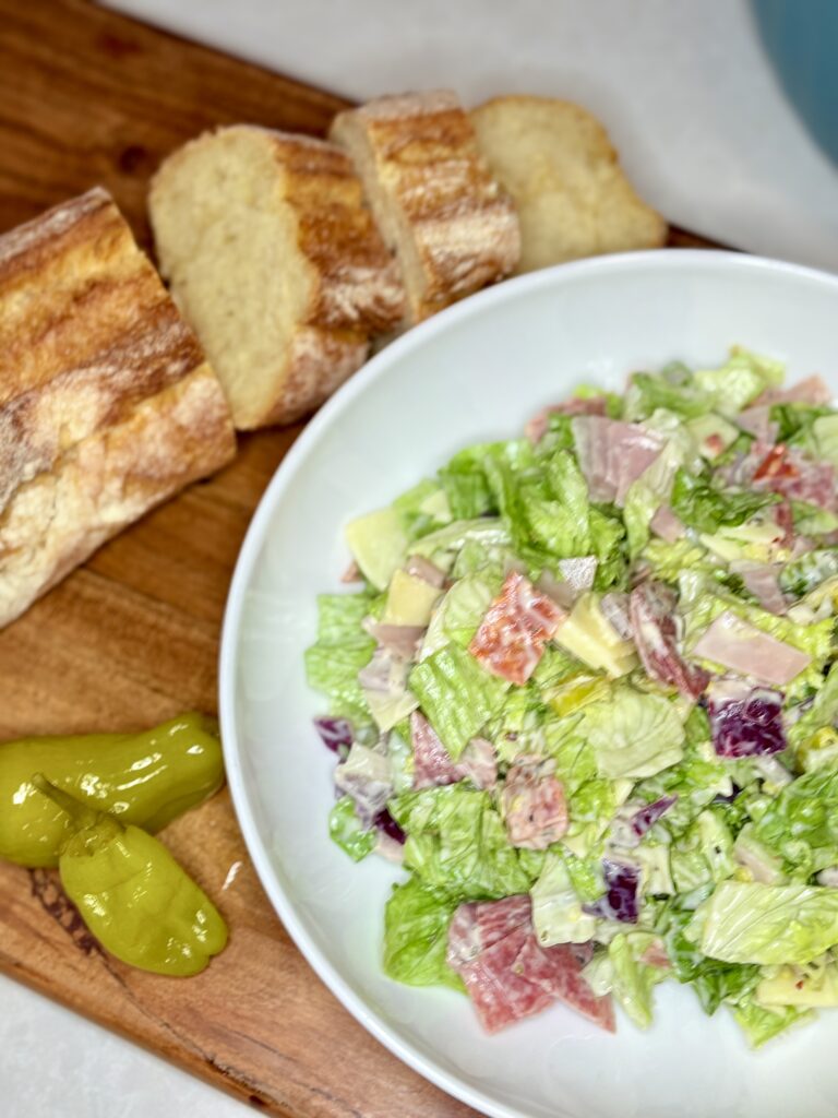 chopped antipasto salad in a meal bowl on a cutting board with a loaf of sliced bread