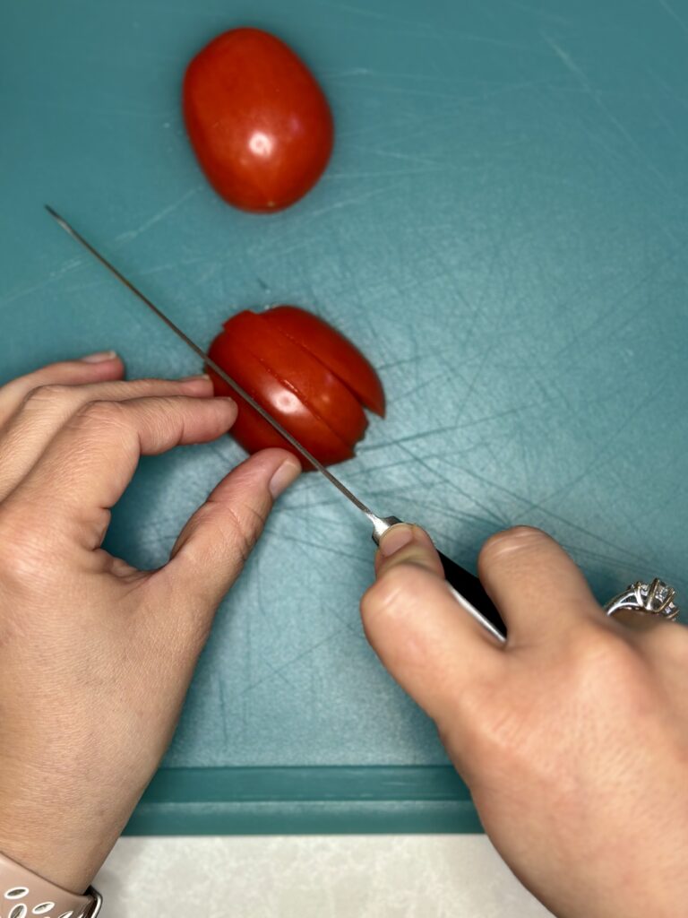 a tomato being sliced in to strips on a cutting board with a knife