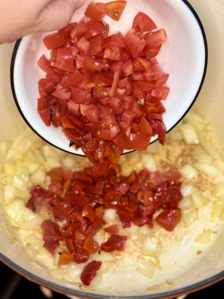 tomatoes and red peppers being added to pot with onions and garlic