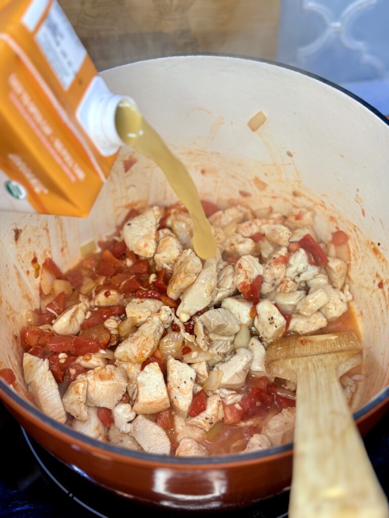 broth being poured in to soup pot with chicken and vegetables