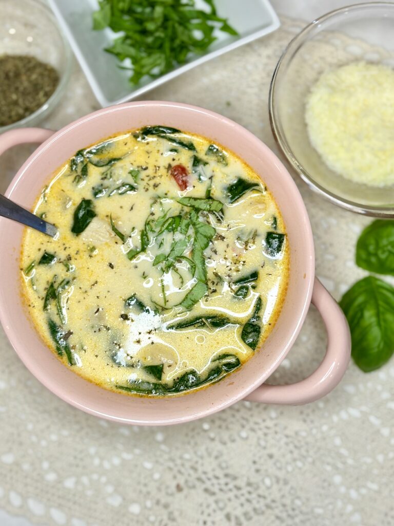 a bowl of creamy chicken Florentine soup on a counter next to bowls of seasoning, fresh basil and parmesan 