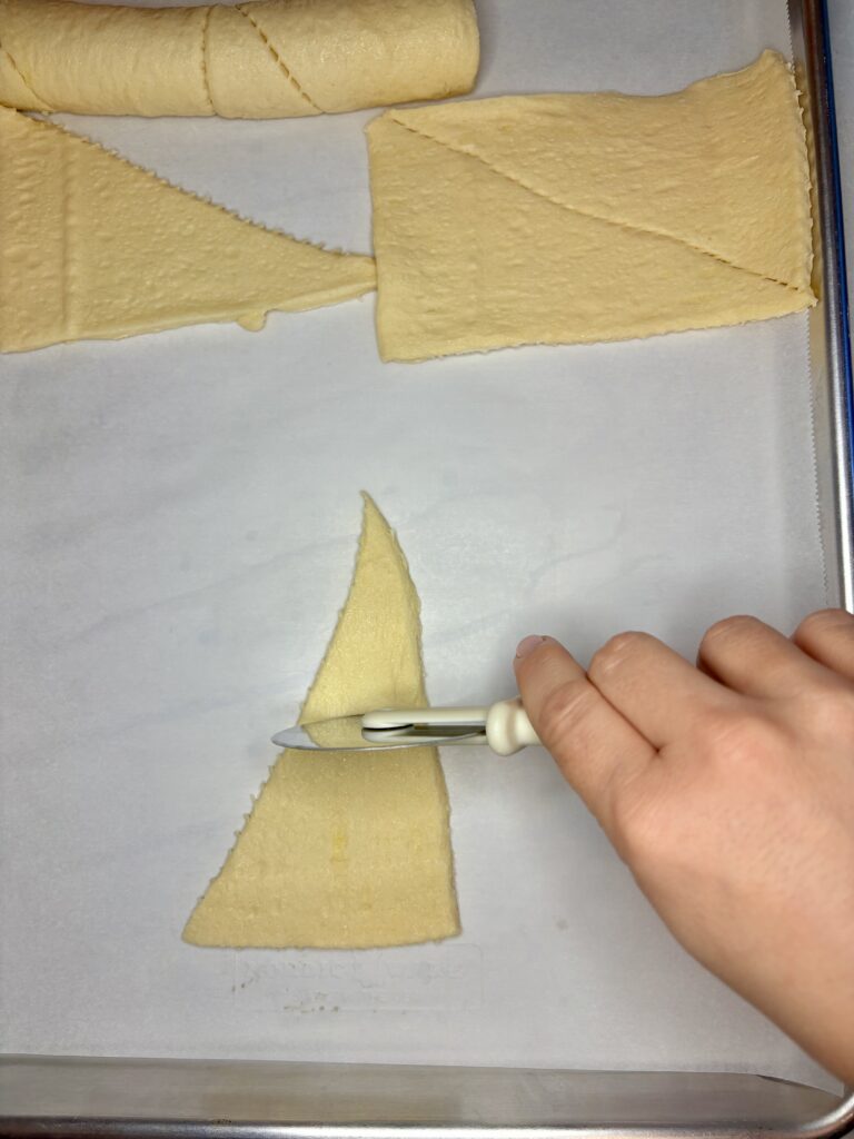 a crescent roll triangle being cut with a pizza cutter