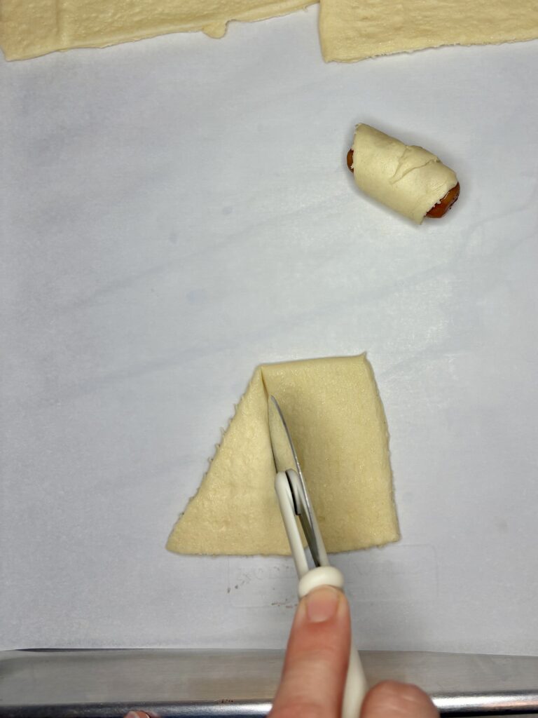 a crescent roll triangle being sliced with a pizza slicer