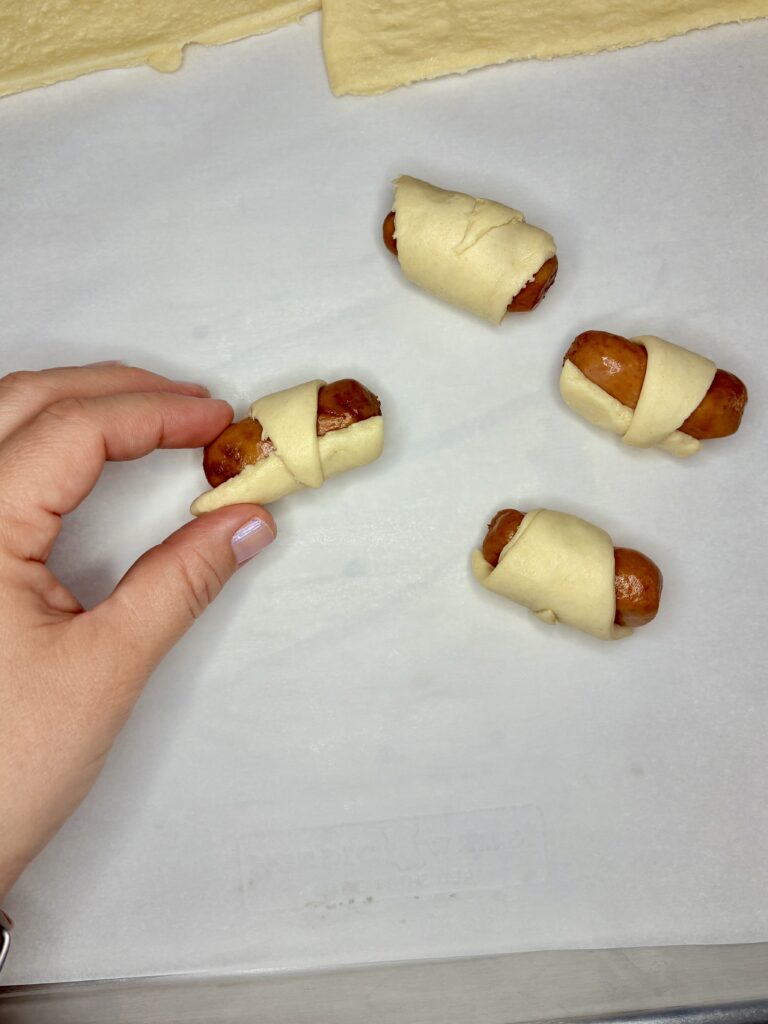 a hand showing a sausage wrapped in a crescent roll