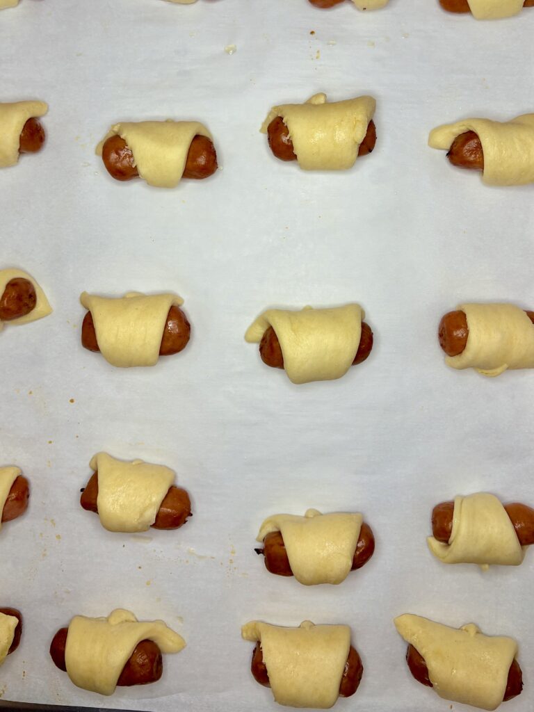 a baking sheet lined with parchment paper with uncooked pigs in a blanket