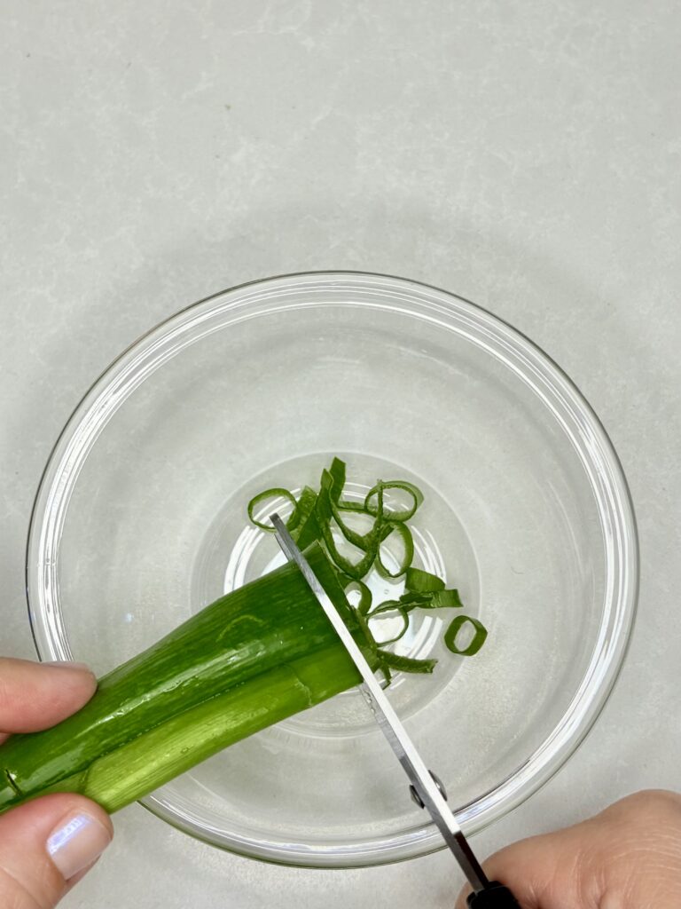 green onions being cut into small strips with scissors in to a bowl