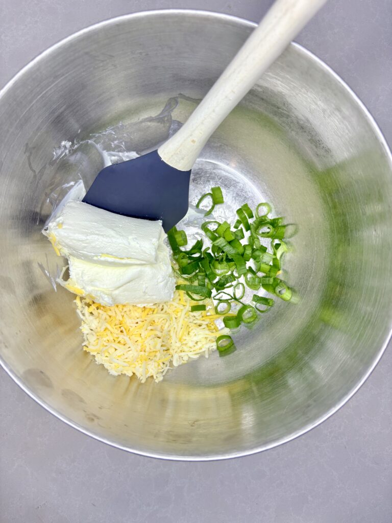 cream cheese, sliced green onions, and shredded cheese in a bowl with a spatula 