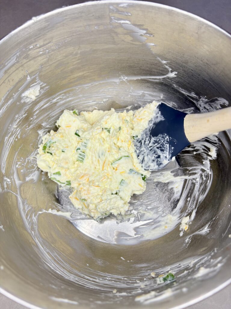 cream cheese, green onions, and shredded cheese mixed together in a bowl with a spatula