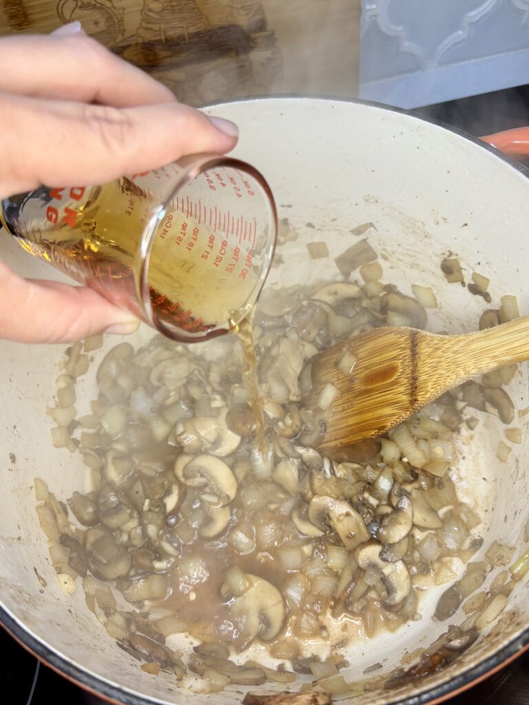 brandy being poured into pot with garlic, onion, and mushrooms