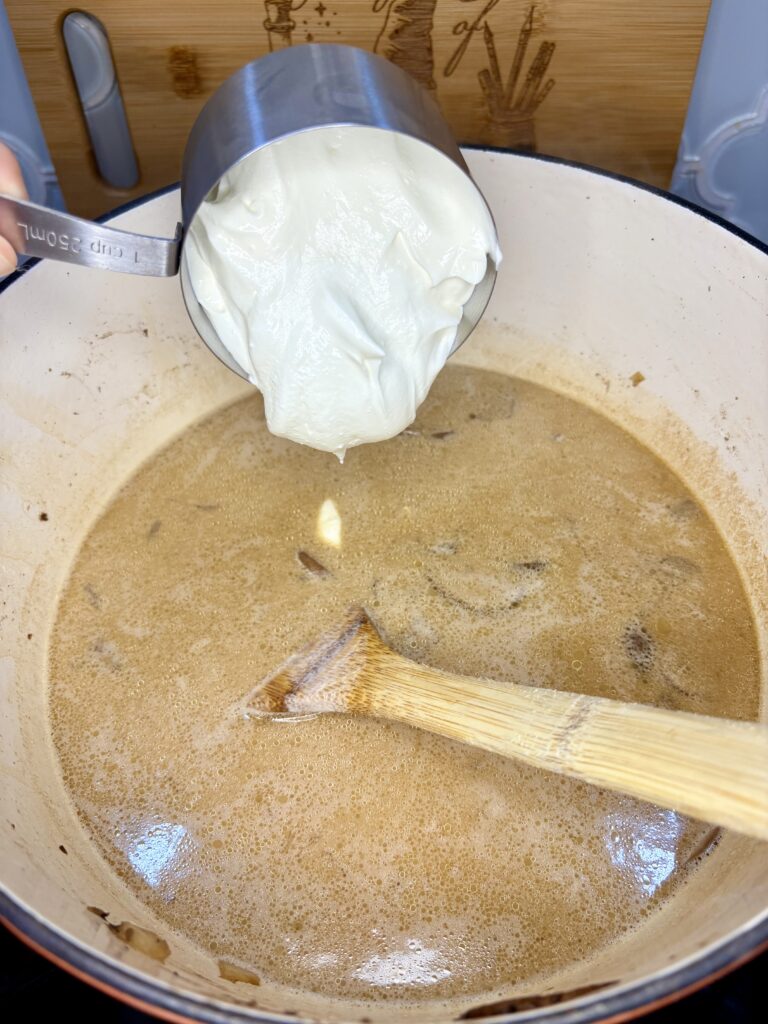 sour cream being added to pot with soup on a stove