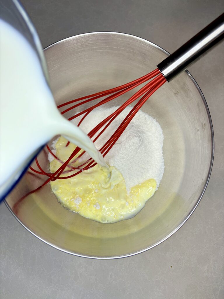 milk being added to a bowl with instant pudding mix and a whisk