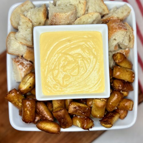 a bowl of beer cheese surrounded by pretzel bites and chunks of bread