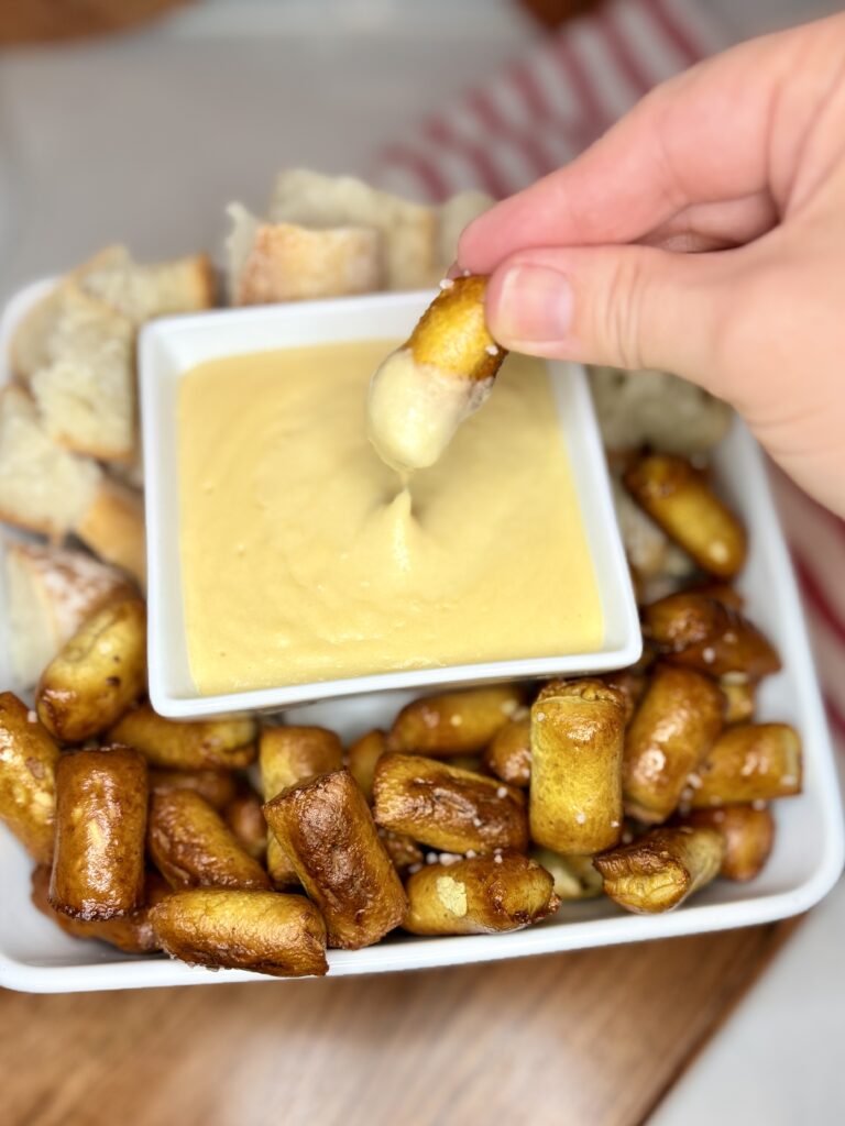 a hand dipping a pretzel bite into a bowl of beer cheese