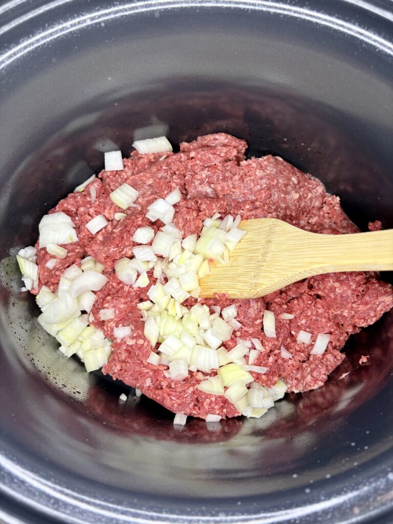 raw ground beef with diced raw onions in a pan on the stove