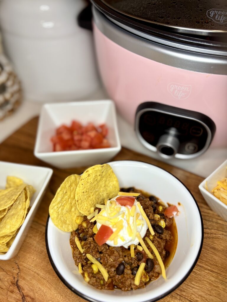 easy game day chili in a bowl next to a slow cooker and bowls of toppings