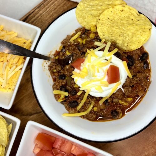 A bowl of chili topped with sour cream, cheese, and tomatoes on a counter