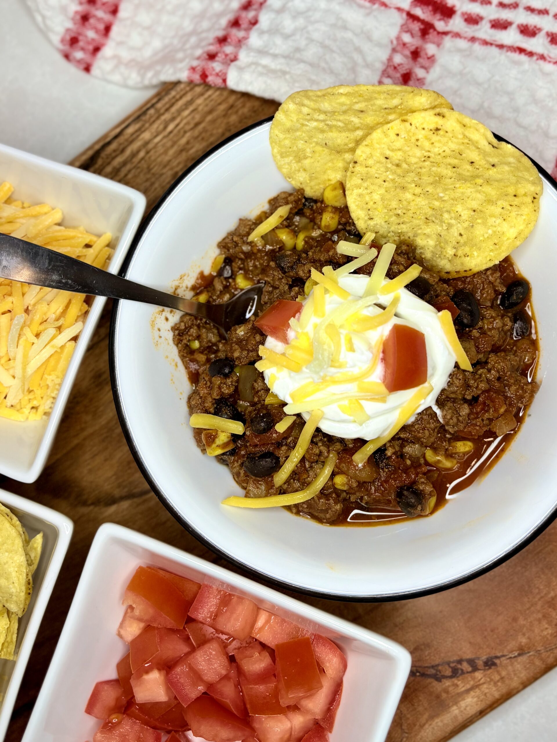 A bowl of chili topped with sour cream, cheese, and tomatoes on a counter