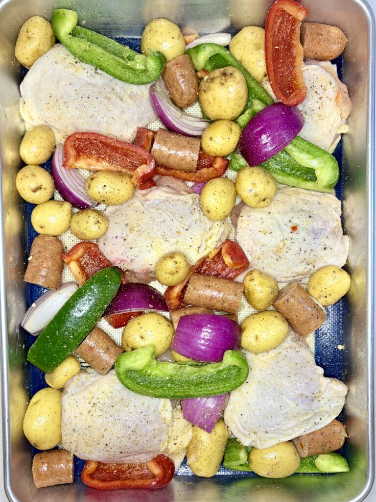 raw vegetables and chicken on a deep sheet pan with sausage and seasoning