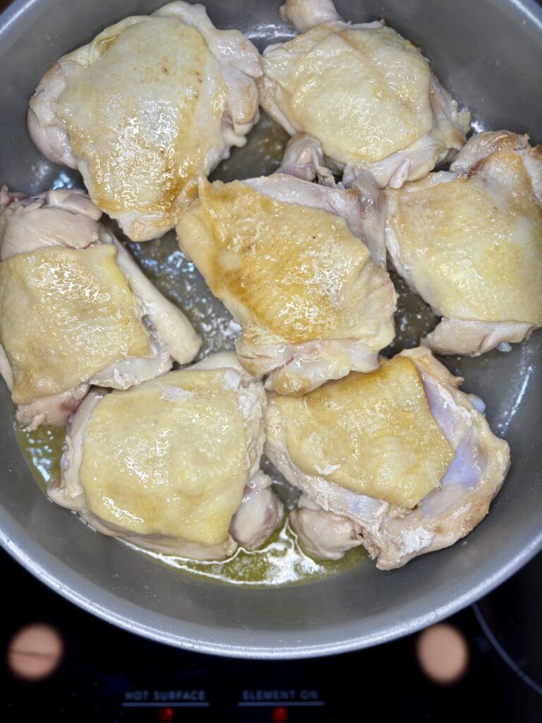 Chicken thighs browning in a skillet on a stove 