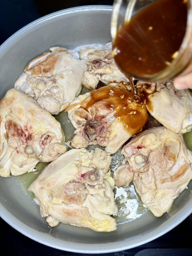 Huli Huil sauce being poured over chicken thighs in a skillet