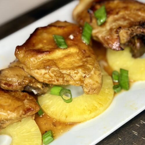 Baked Huil Huli Chicken on a plate with pineapple slices and green onions