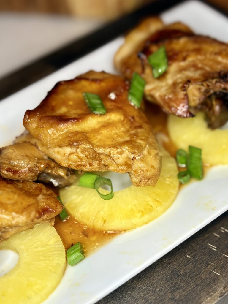 baked huli huli chicken on a plate with pineapple slices and green onions