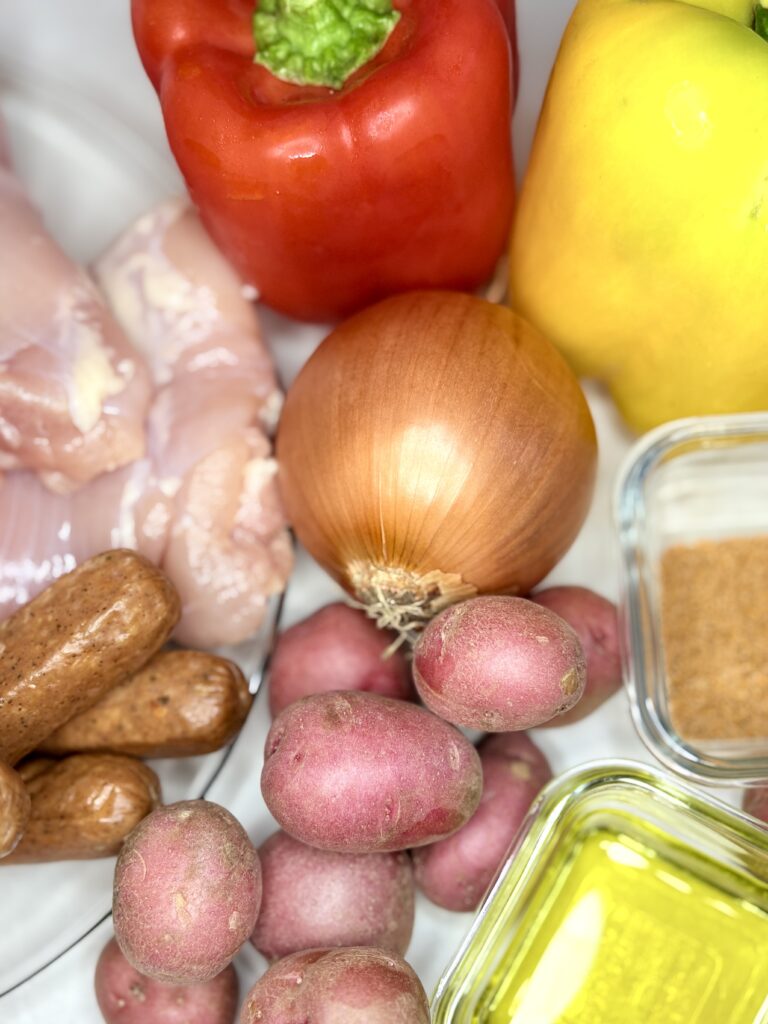 chicken, sausage, peppers, potatoes, onion, seasoning, and olive oil on a counter