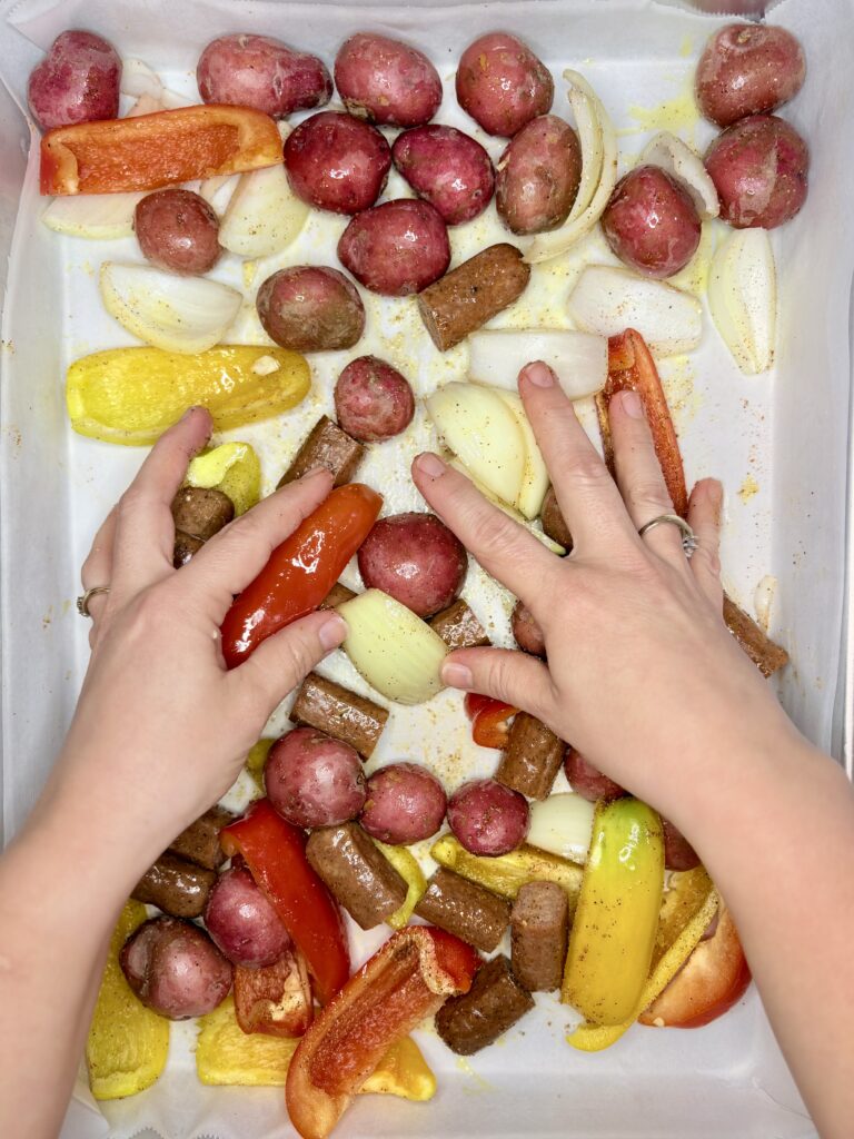 hands mixing the vegetables and sausage together with oil and seasoning