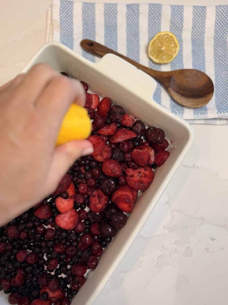 Mixed berries in a white baking dish with lemon beans squeezed on top