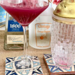 Blueberry and Pineapple Margarita cocktail with fresh blueberries garnished on top, served in a martini glass on patterned coasters, featuring tequila, orange liqueur, and vibrant pink color, perfect for summer drinks.