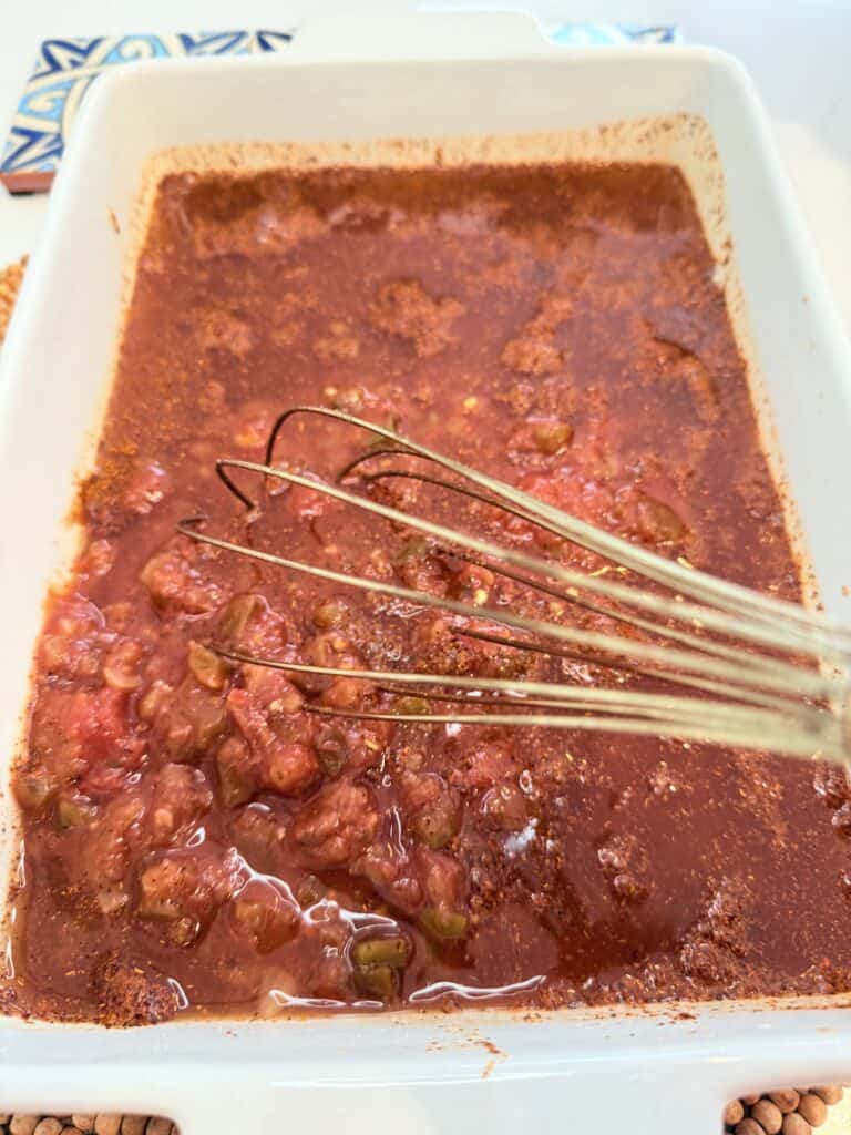 Whisking together the salsa and the taco seasoning and a white casserole dish on the counter.