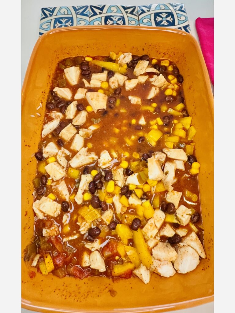 The diced pieces of chicken and the chopped yellow bell pepper and the drained black beans to the 2 cups of water, the salsa, and the  taco seasoning blend in an orange casserole dish on the counter.