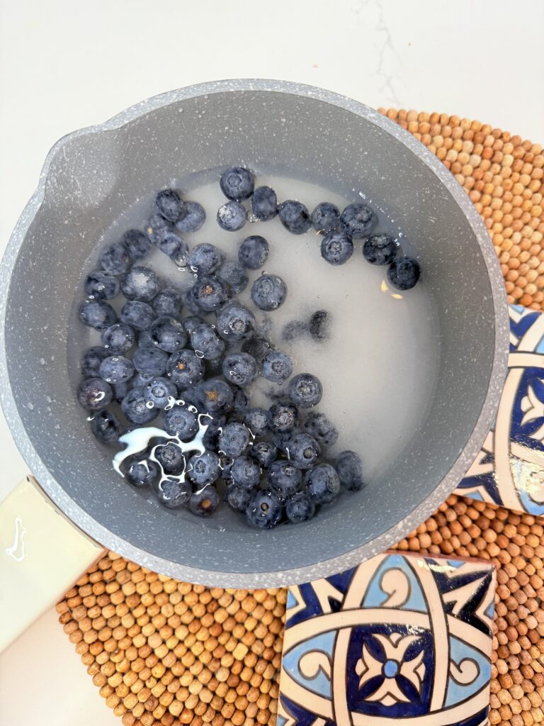 Blueberries, water, and sugar in a pot on a brown mat on the counter.