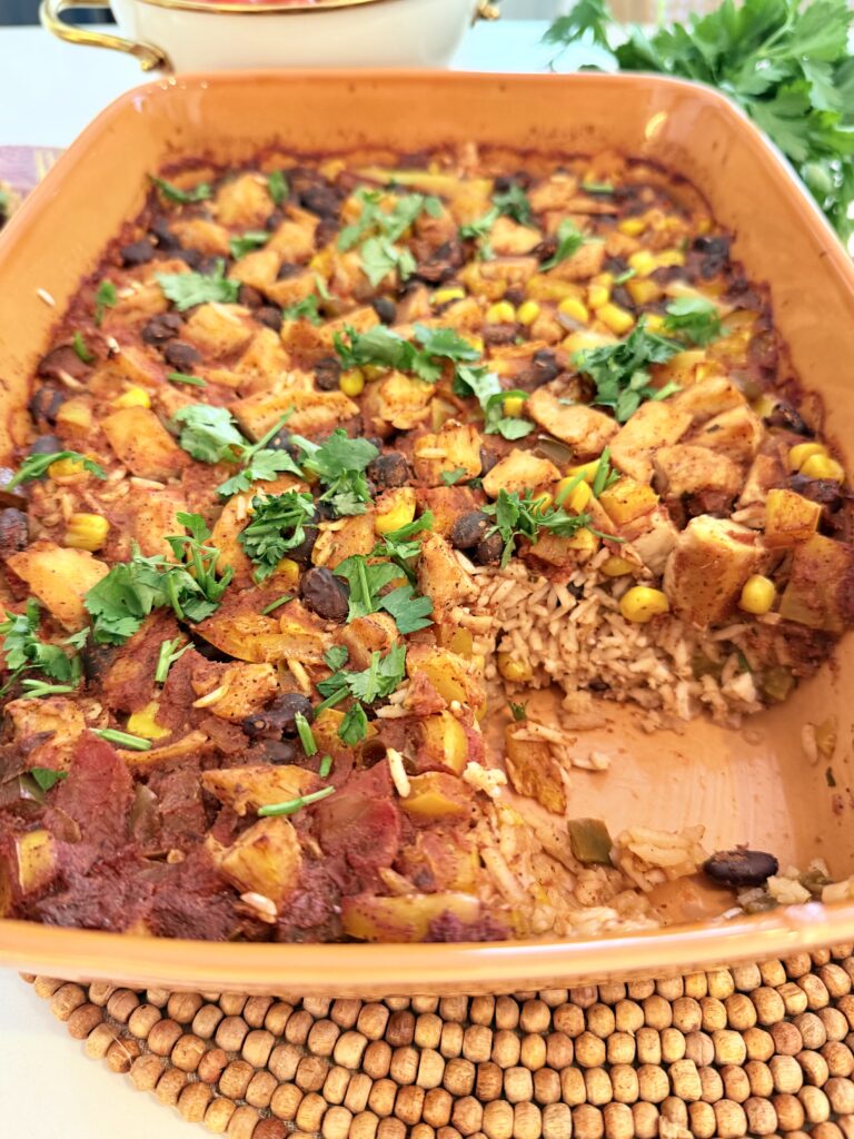 One pan taco chicken casserole in an orange casserole dish on the counter with one piece missing.