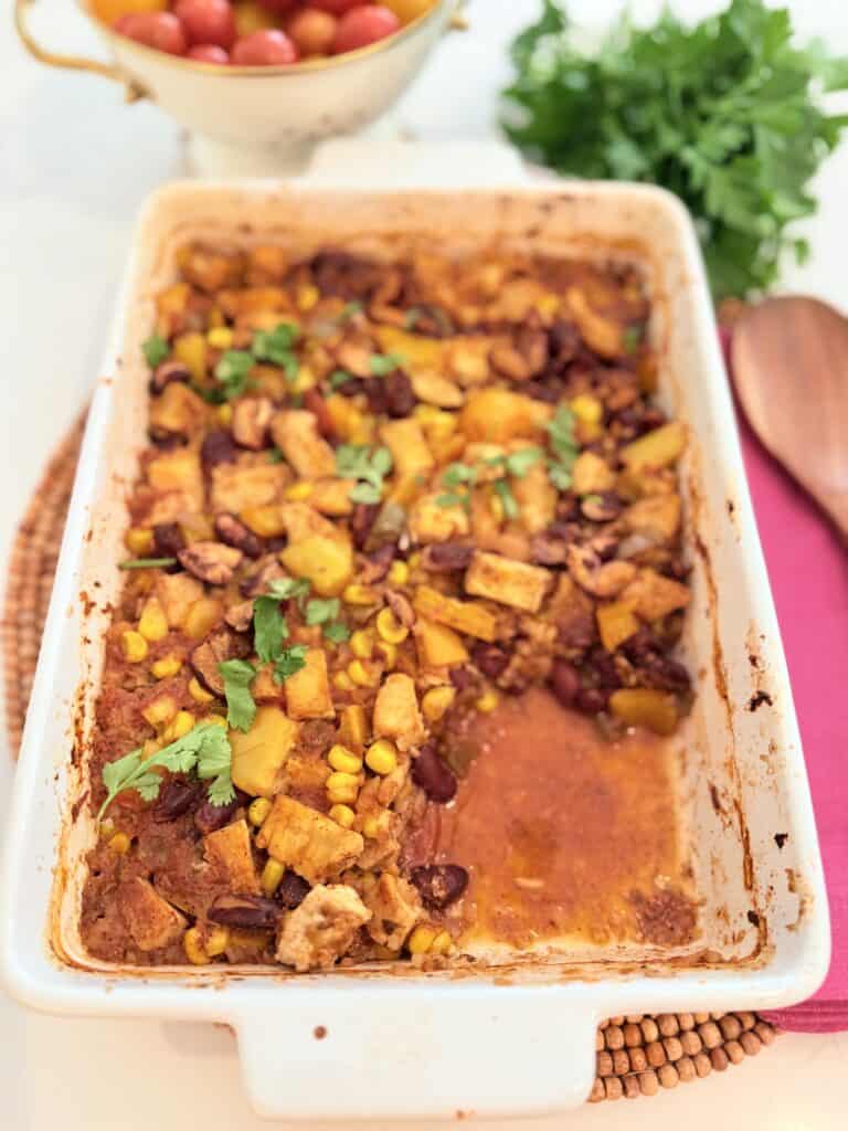 Low-carb taco chicken casserole in a white casserole dish in the foreground is a piece of the low-carb taco chicken casserole missing on the counter.