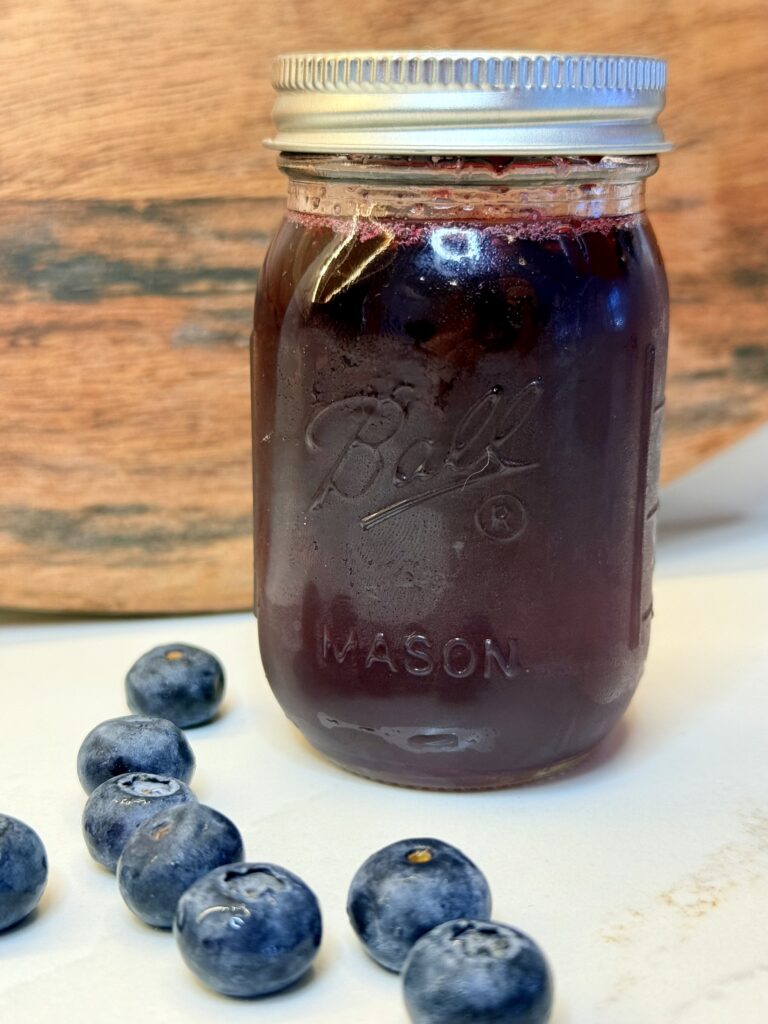 Cooled and strained blueberry, simple syrup in a glass container on the counter.