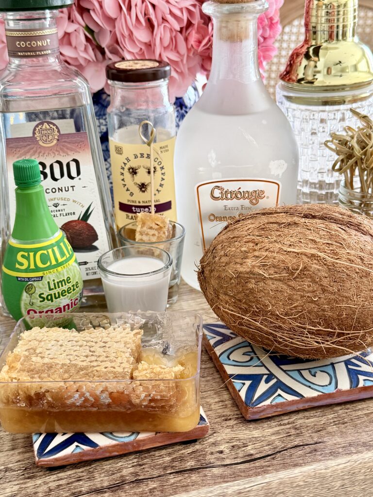 Coconut tequila, honey syrup, coconut cream, lime juice, orange liqueur, honeycomb, and coconut on a brown tray on the counter.