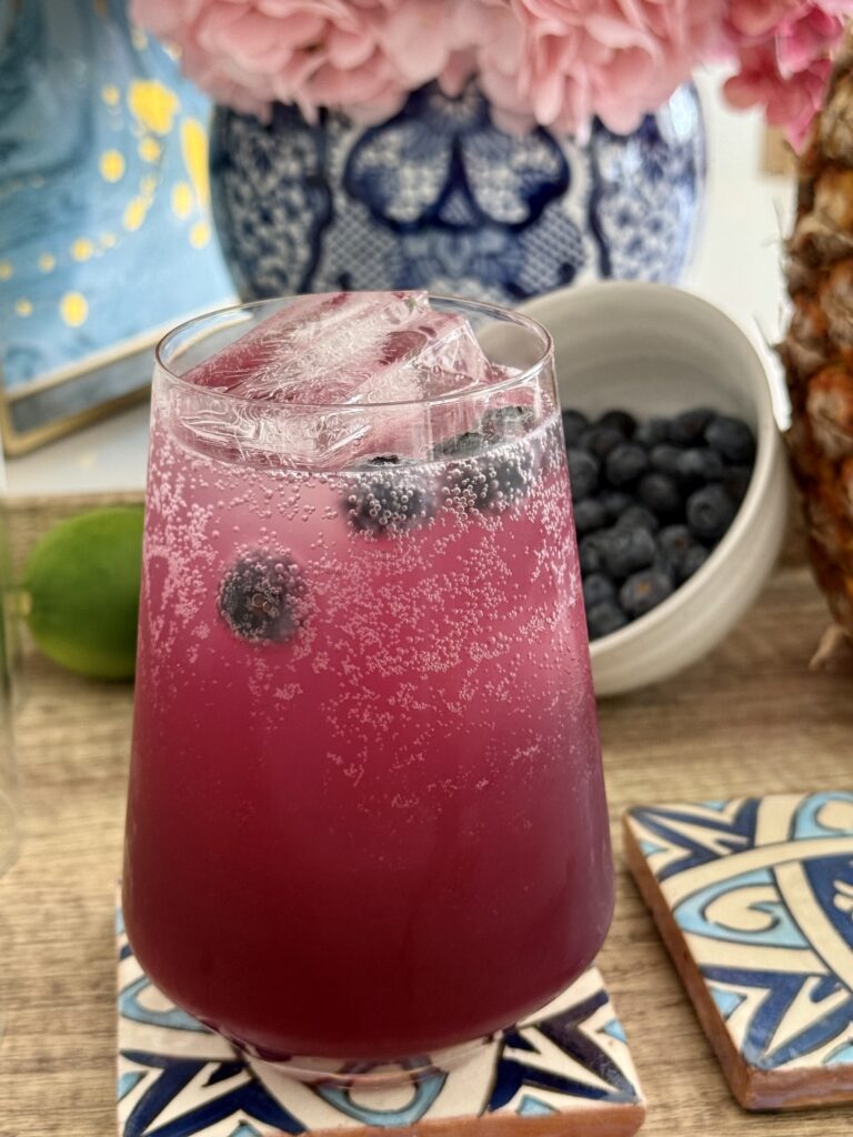 Blueberry and Pineapple mocktail on a blue coaster on a brown tray on the counter.