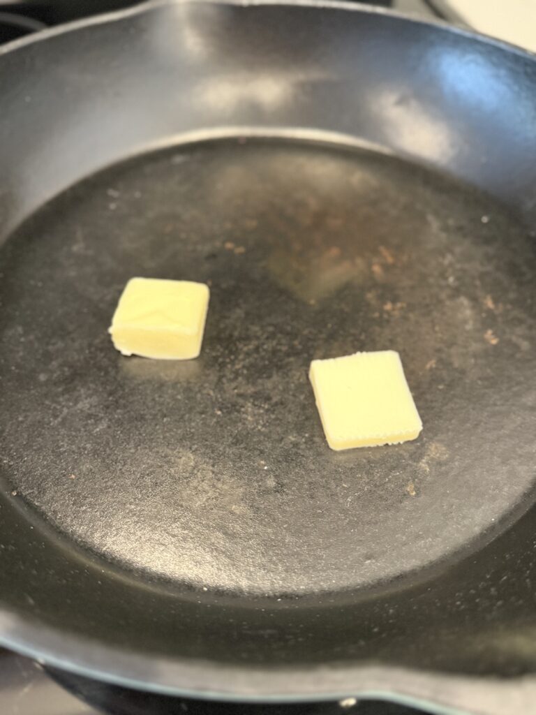 two tabs of butter in a black cast iron skillet on the stove top.