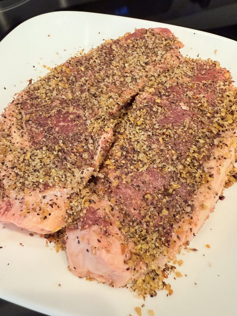 Seasoned steaks on a white plate on the stove top.