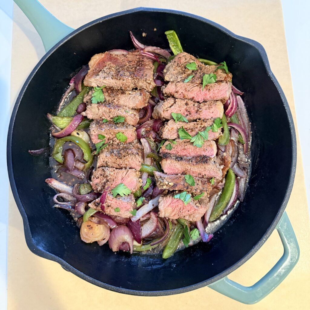 Steak, Onion, and Pepper one-pan dinner in a black cast-iron skillet on brown parchment paper on the counter.