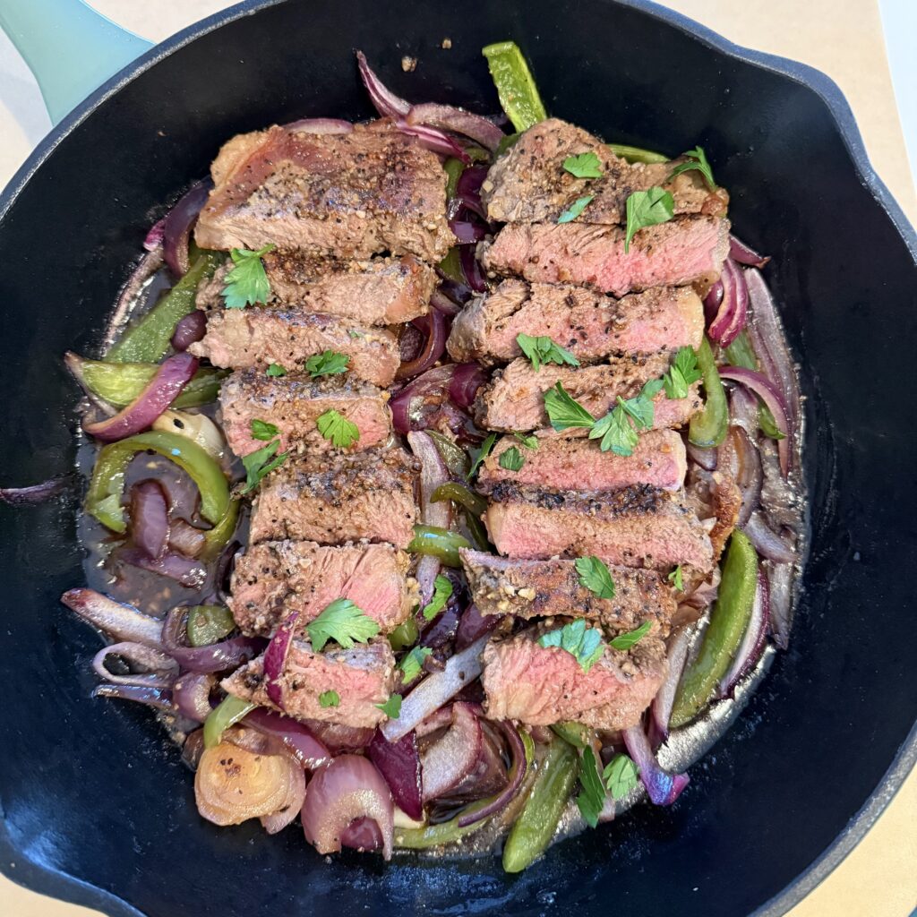 Sliced steaks, place them back on the roasted vegetables, and garnish with fresh parsley for a pop of vibrant green in a black cast -iron skillet on the counter.